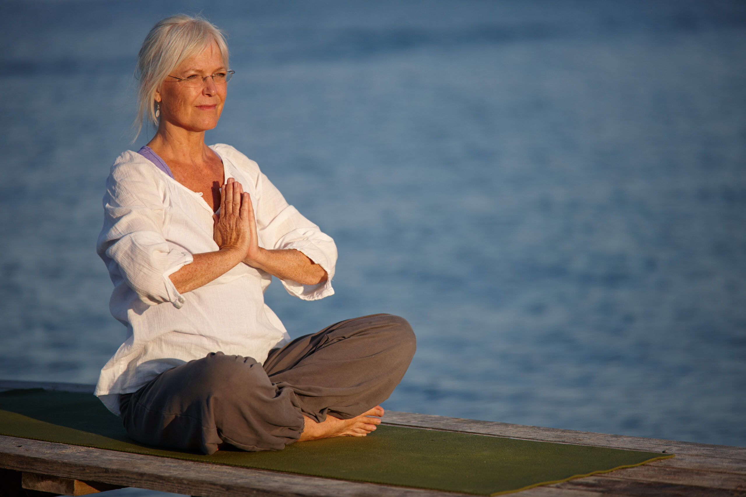 Tranquility by the ocean. Shot of an attractive mature woman doing yoga on a pier out on the ocean. Depositphotos 551379412 XL scaled